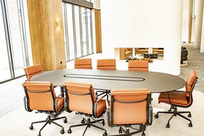 A conference room with a round table and six chairs, large windows, and a wooden accent wall.
