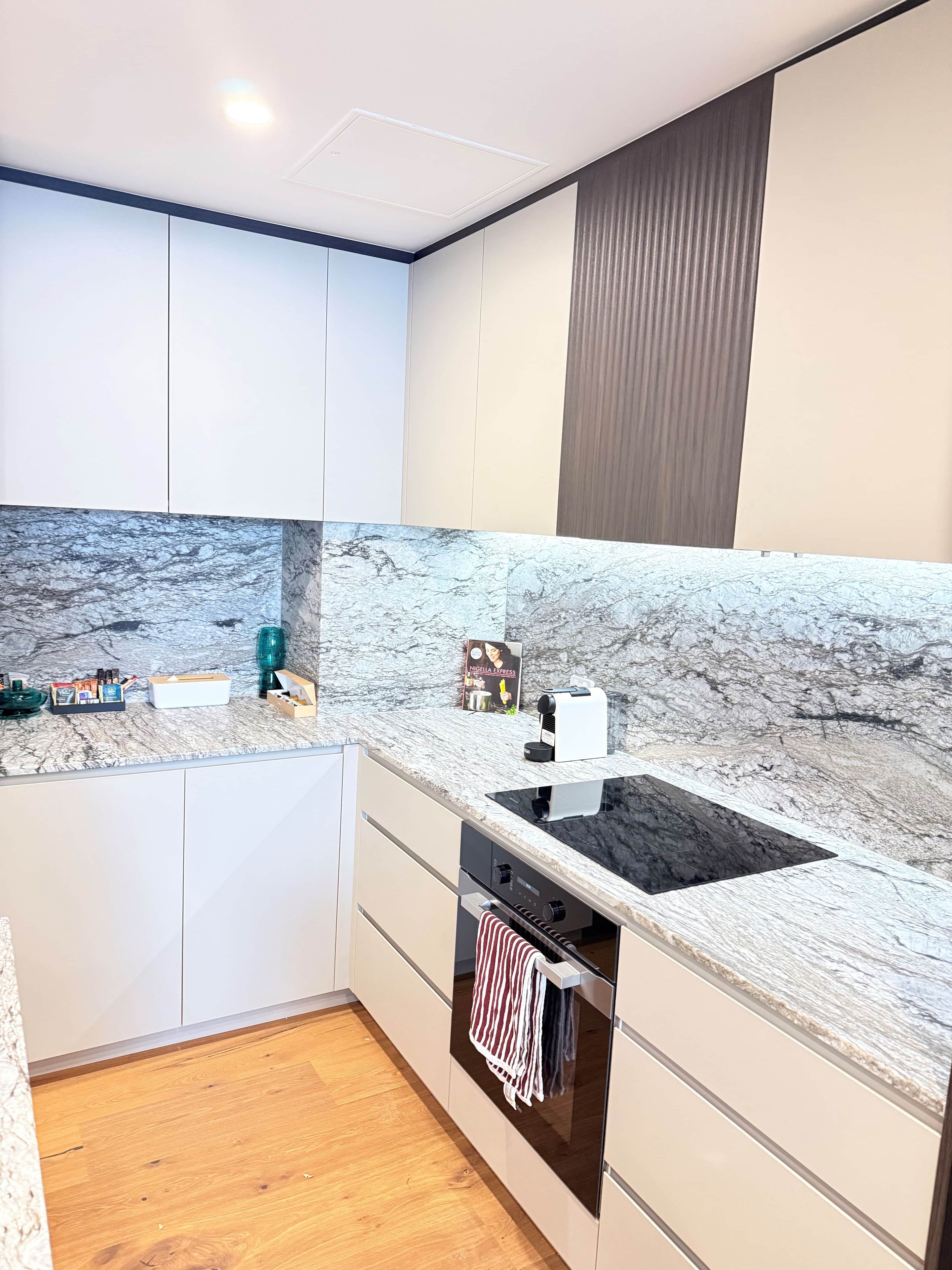 A modern kitchen with a marble countertop, built-in oven, and white cabinetry.
