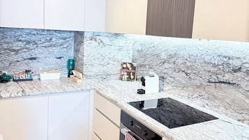 A modern kitchen with a marble countertop, built-in oven, and white cabinetry.