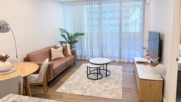 A modern living room with a brown leather sofa, a round dining table, and a TV on a stand.