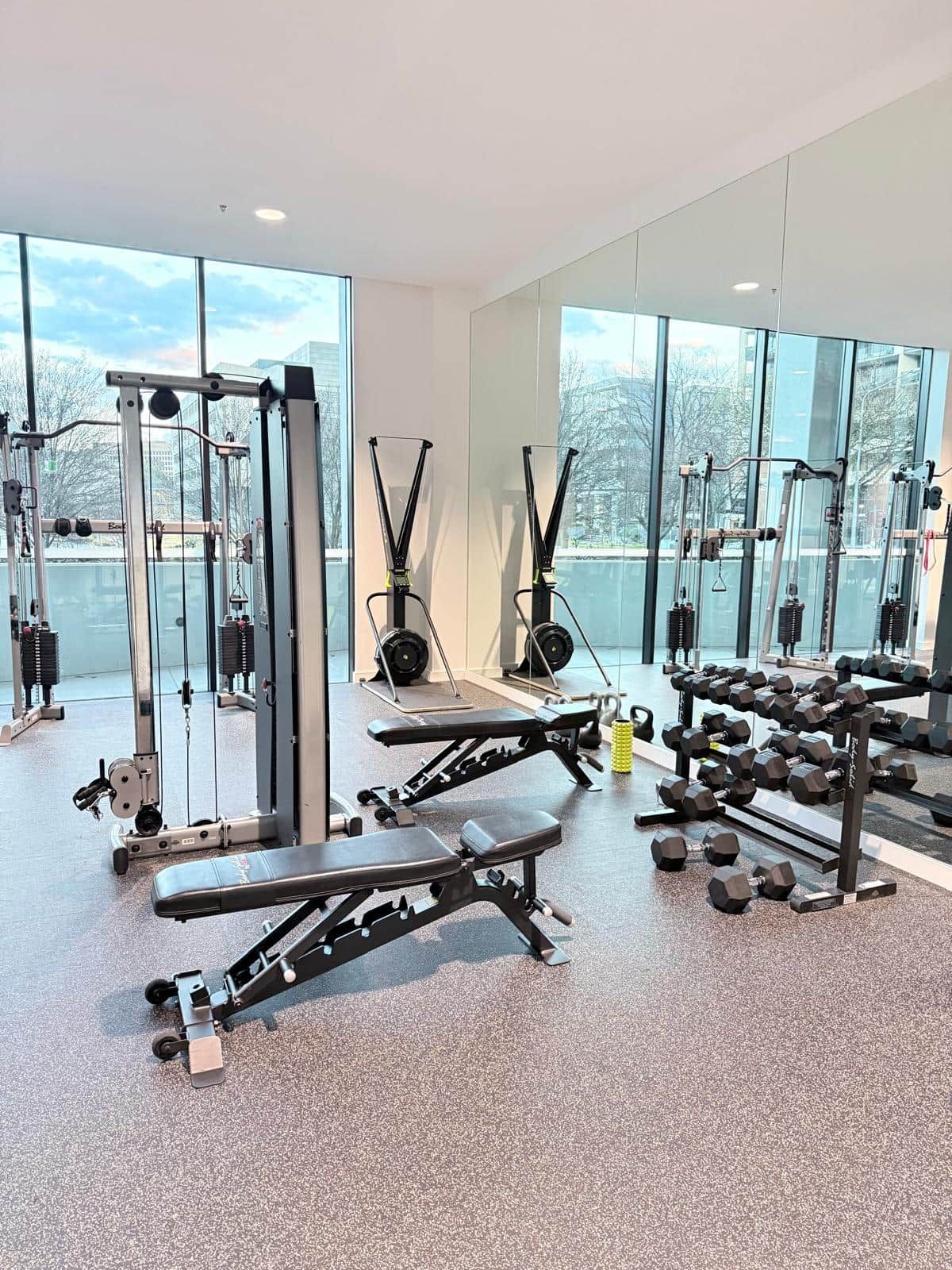 A gym with various exercise equipment, large windows, and a view of the outside.