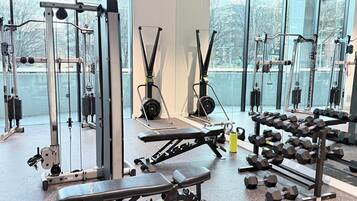A gym with various exercise equipment, large windows, and a view of the outside.