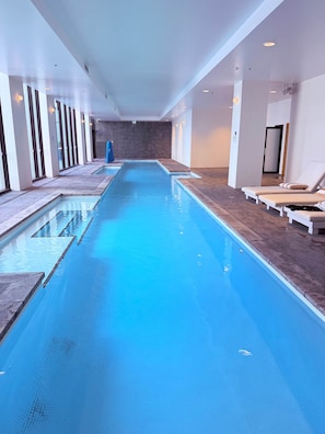 En lang, indendørs swimmingpool med krystalklart vand, omgivet af liggestole og moderne indretning.