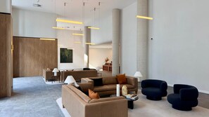 A spacious lobby with a modern design, featuring a seating area with sofas and armchairs, a reception desk, and a large abstract painting on the wall.