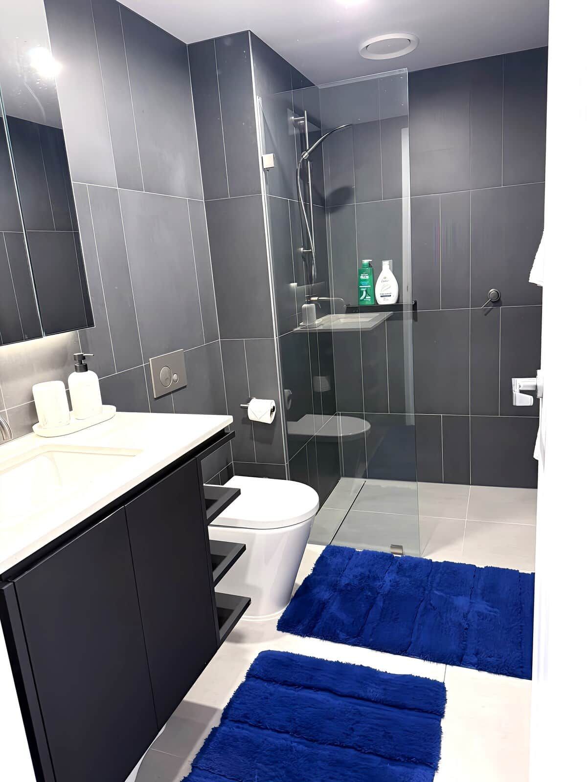 A modern bathroom with a glass shower enclosure, a white toilet, and a black vanity.