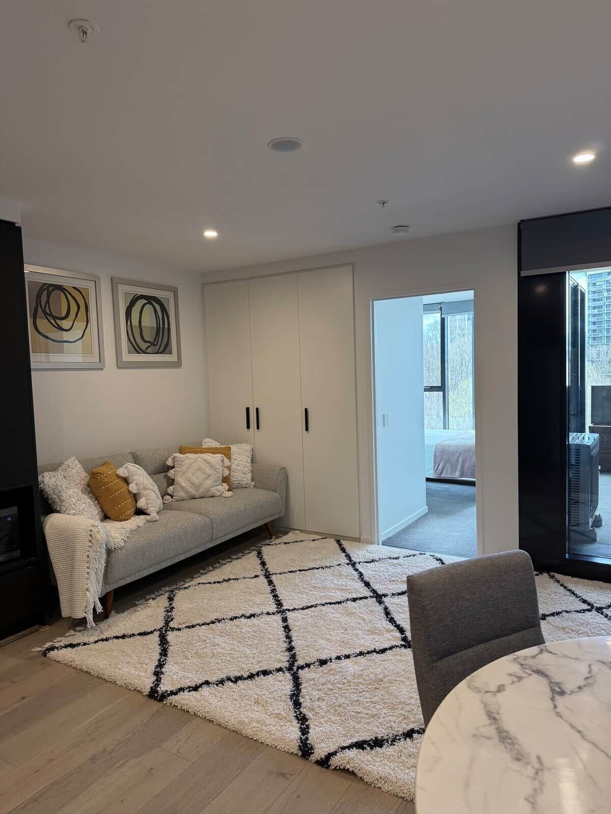 A modern living room with a grey sofa, a white rug, and a marble coffee table.