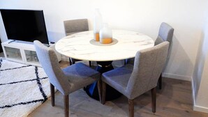A dining area with a round table, four grey upholstered chairs, a white marble table base, and two glass bottles on the table. - Stylish, Cosy City Retreat in Reid Canberra (Reid)