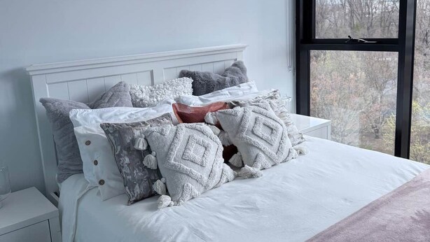 A bedroom with a large bed, a nightstand, a window with a view, and a painting on the wall. - Stylish, Cosy City Retreat in Reid Canberra (Reid)