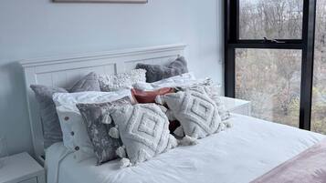 A bedroom with a large bed, a nightstand, a window with a view, and a painting on the wall.