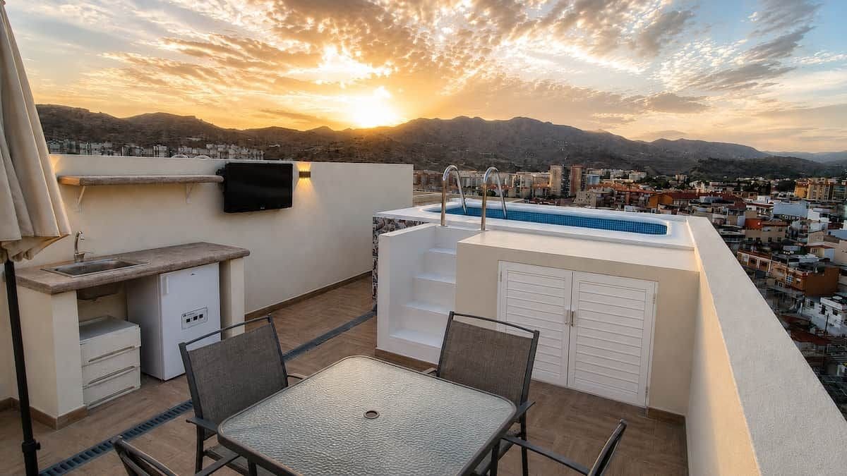 Eine Dachterrasse mit Pool, Sitzgelegenheit und Blick auf die Stadt bei Sonnenuntergang.