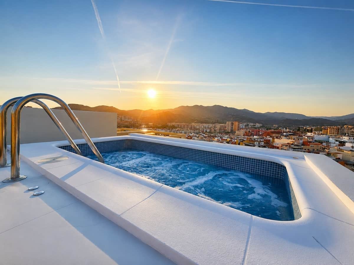 A hot tub with a cityscape view, a metal ladder, and a clear sky.
