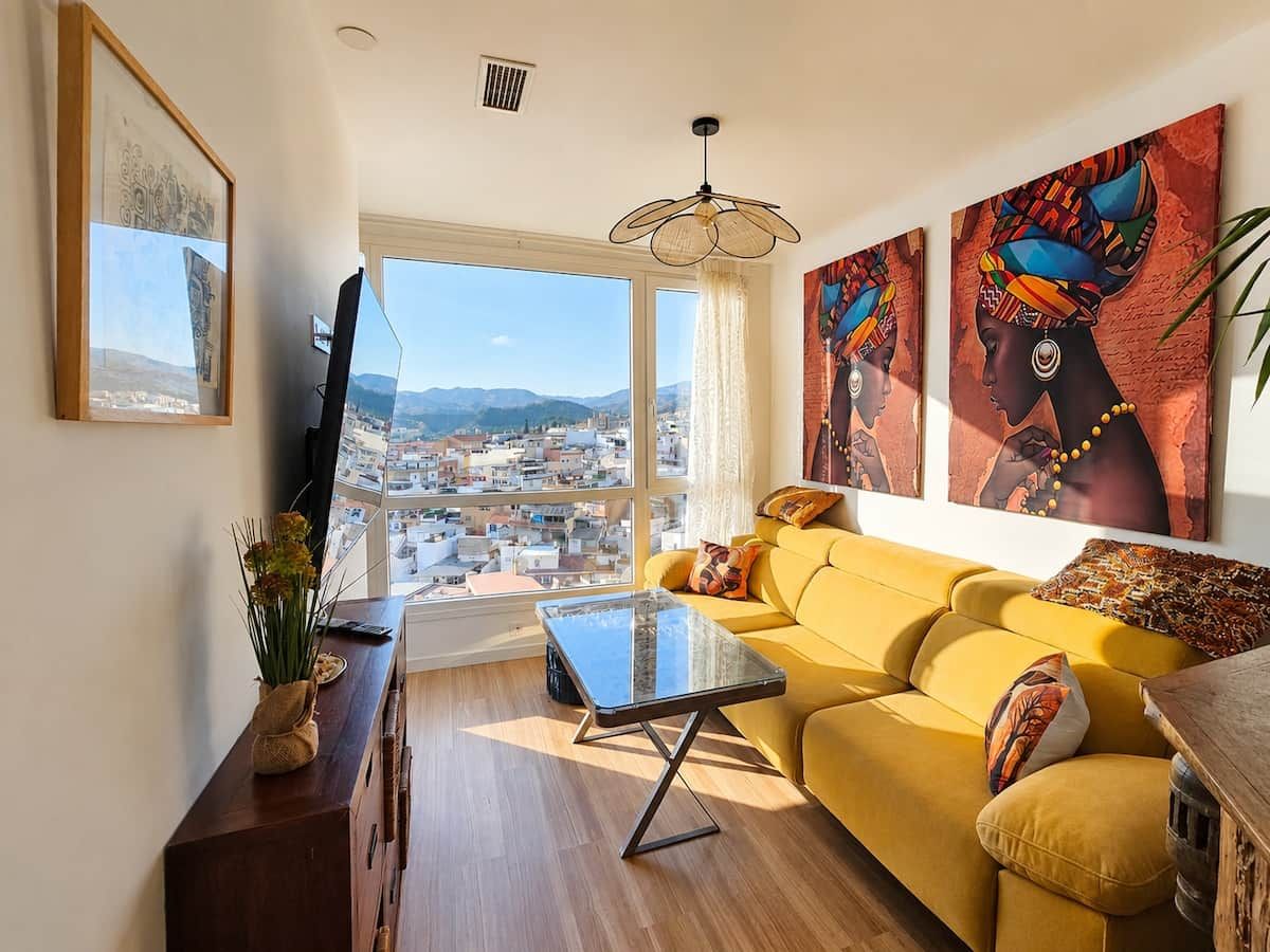 Ein Wohnzimmer mit einer Couch, einem Couchtisch und Blick auf eine Stadtlandschaft durch große Fenster.