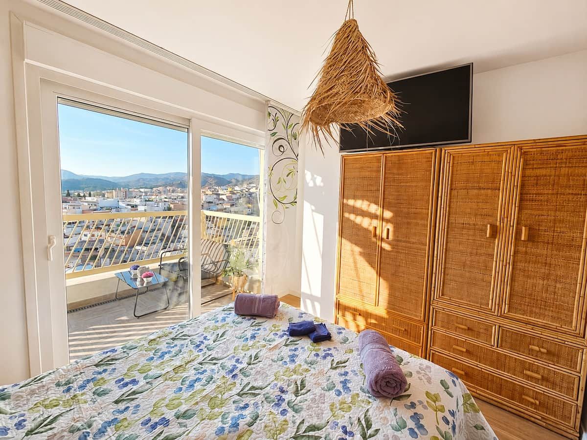 Ein Schlafzimmer mit Bett, Kleiderschrank und einem Balkon mit Blick auf die Stadt.