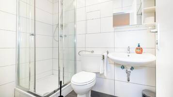 Een moderne badkamer met een glazen douchecabine, een wit toilet en een wastafel met zeepdispenser.
