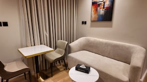 Ett modernt hotellrum med en soffa, ett litet bord, en stol och en tavla på väggen.