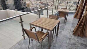 Terrassa al terrat amb barana de vidre, taula i cadires, i vista a la ciutat.