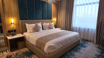 A hotel room with a large bed, bedside lamps, a telephone, and a view of the outdoors through sheer curtains.