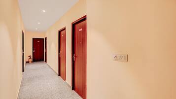 A hotel corridor with carpeted floors, wooden doors, and a light switch on the wall.