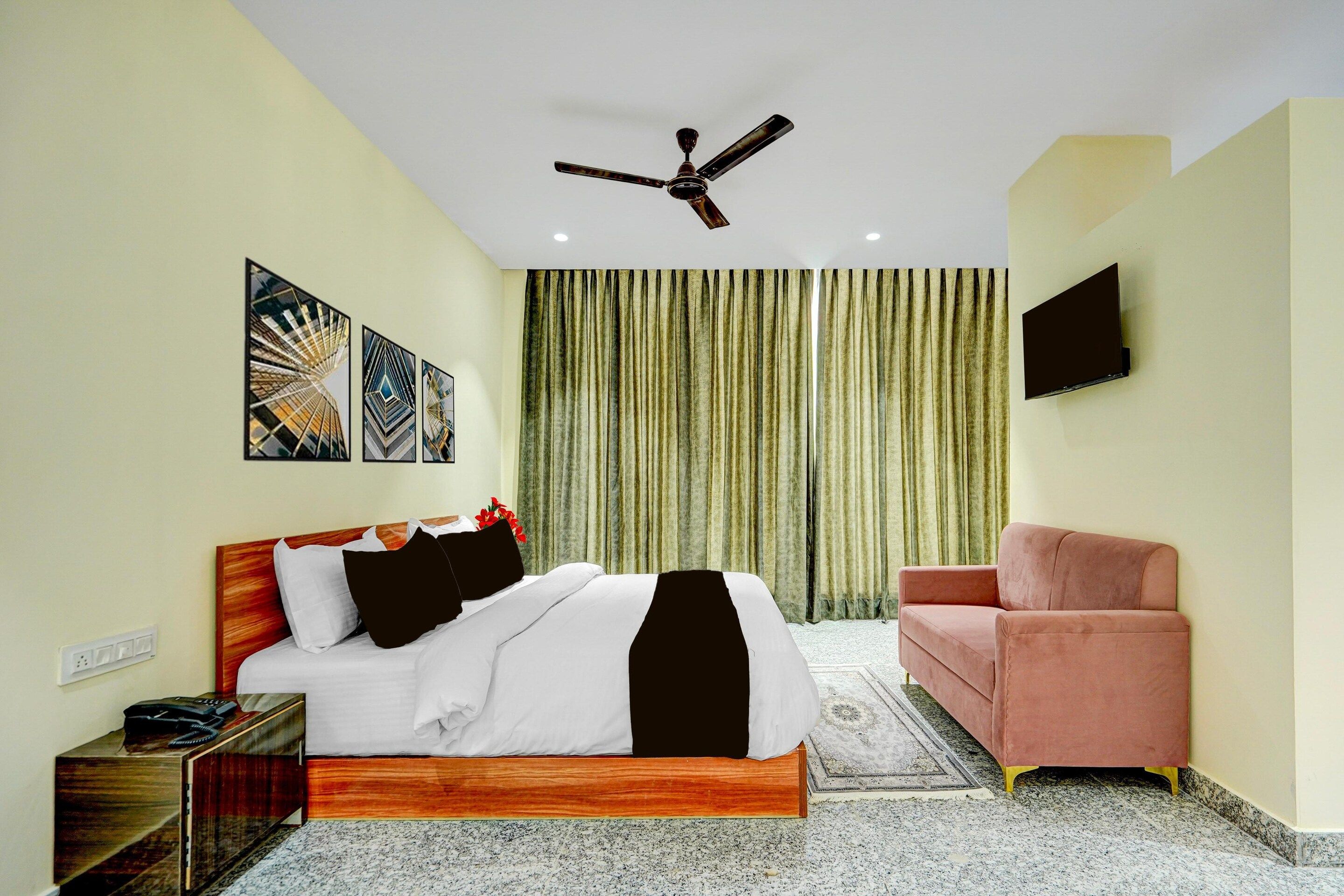 A hotel room with a bed, a desk, a chair, a ceiling fan, and a TV mounted on the wall.