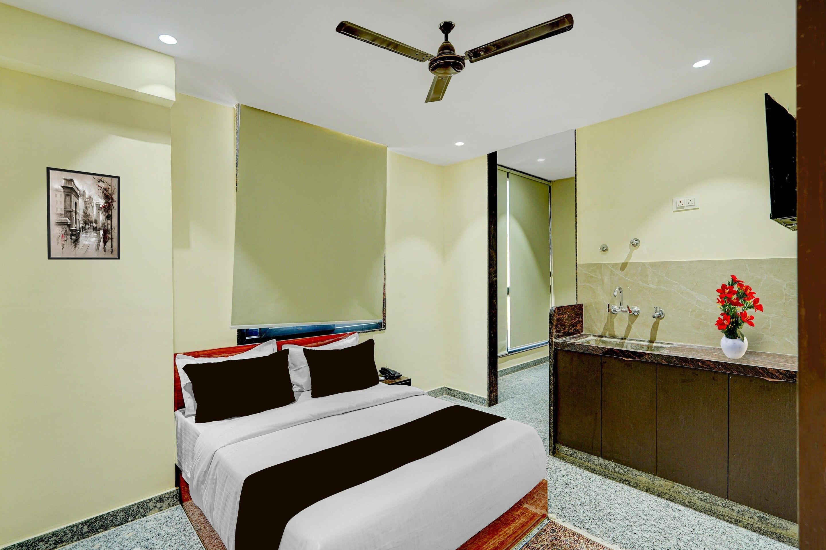A hotel room with a bed, a ceiling fan, a bathroom with a sink and mirror, and a framed picture on the wall.