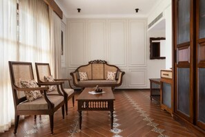 A room with a wooden floor, a sofa, two armchairs, a coffee table, and a cabinet. - Sanskreti (Kochi)