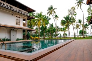 A swimming pool adjacent to a building with a balcony, surrounded by palm trees. - Sanskreti (Kochi)