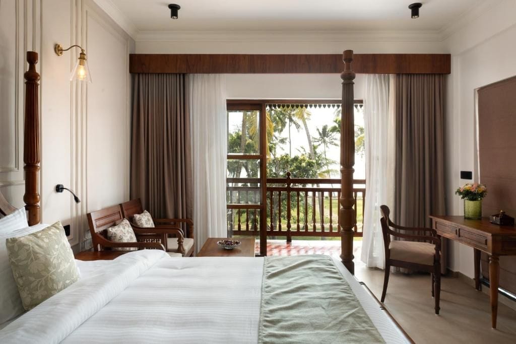 A hotel room with a large bed, a desk, a chair, and a balcony with curtains.