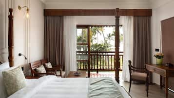 A hotel room with a large bed, a desk, a chair, and a balcony with curtains.