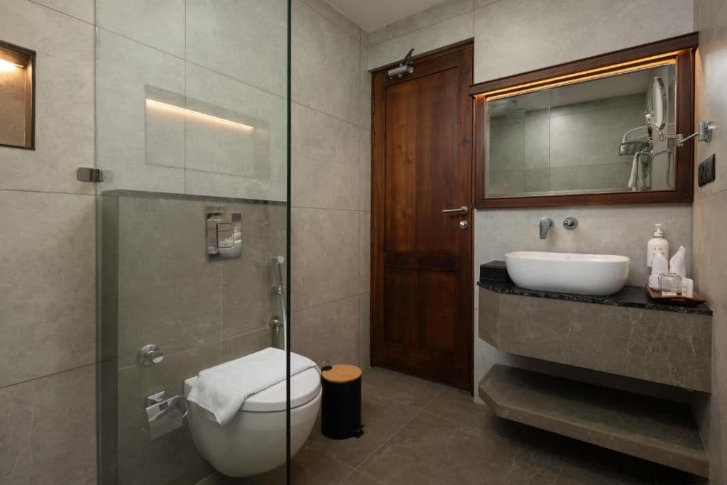 A modern bathroom with a glass-enclosed shower, a wooden door, a white sink, and a mirror above the sink.