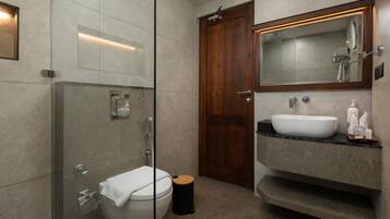 A modern bathroom with a glass-enclosed shower, a wooden door, a white sink, and a mirror above the sink.