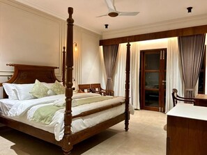 A four-poster bed with a wooden headboard, a ceiling fan, and a view of a sliding glass door leading to a balcony. - Sanskreti (Kochi)