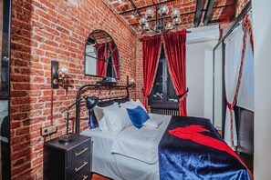 A room with a brick wall, a bed with white bedding, a black metal headboard, a black nightstand with a lamp, and red curtains. - Allegory of Taksim 2B (İstanbul)