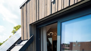 Un bâtiment moderne doté d’une façade en bois, d’une entrée avec une porte en verre et d’un intérieur visible, comprenant un espace repas.