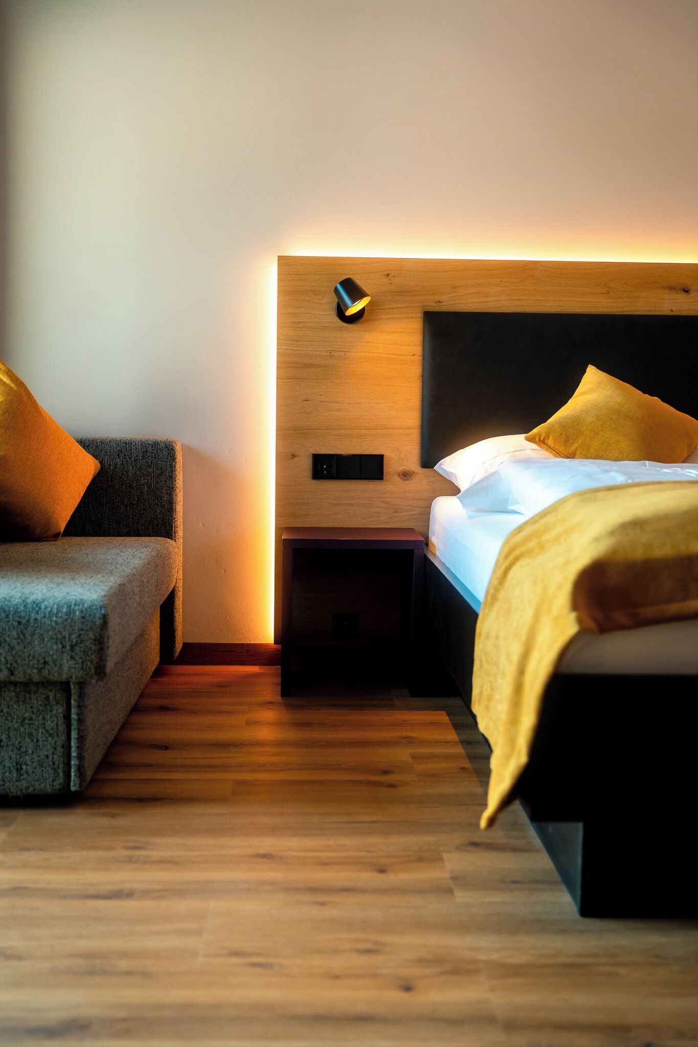 A modern bedroom with a wooden headboard, a bedside table, and a sofa.