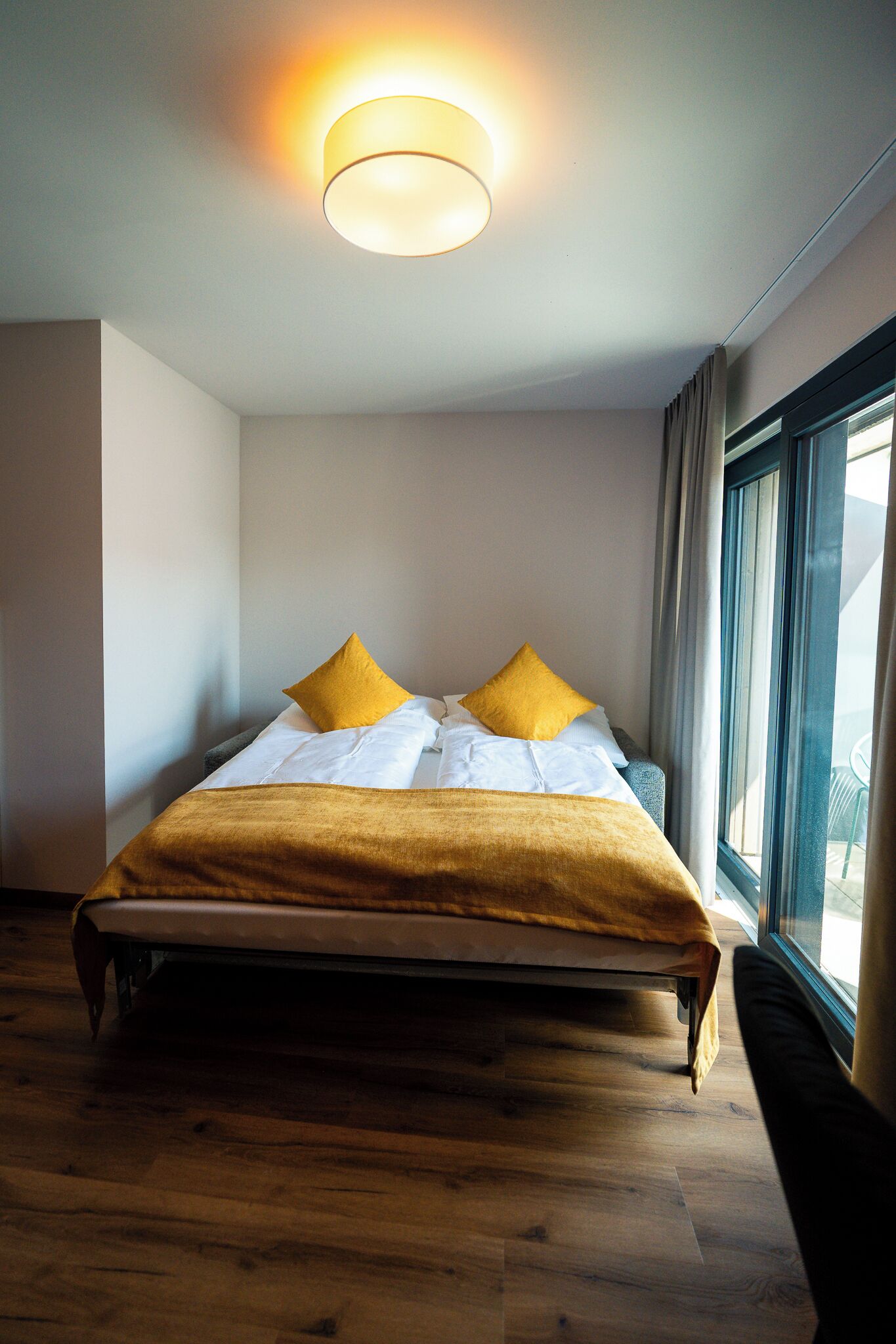 Ein modernes Hotelzimmer mit einem großen Bett, einem Vorhangfenster und einer Deckenleuchte.