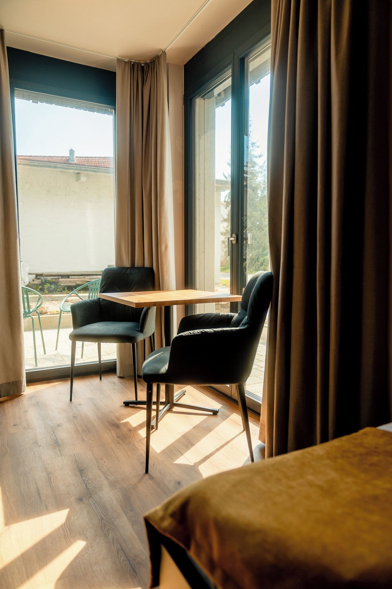 A room with a wooden floor, a table, two chairs, and a view through a window with curtains.