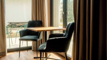 A room with a wooden floor, a table, two chairs, and a view through a window with curtains.