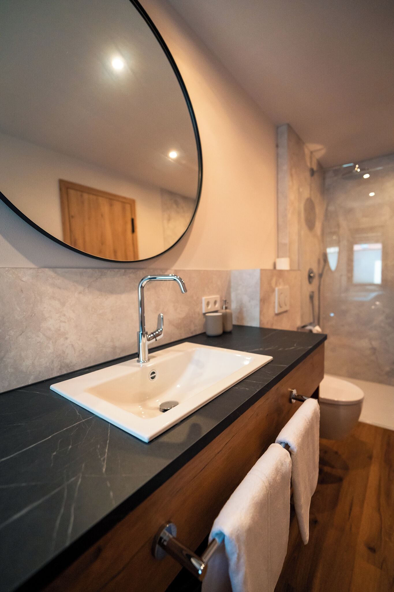 Ein modernes Badezimmer mit einem weißen Waschbecken, einem großen Spiegel und einer Holzausstattung.