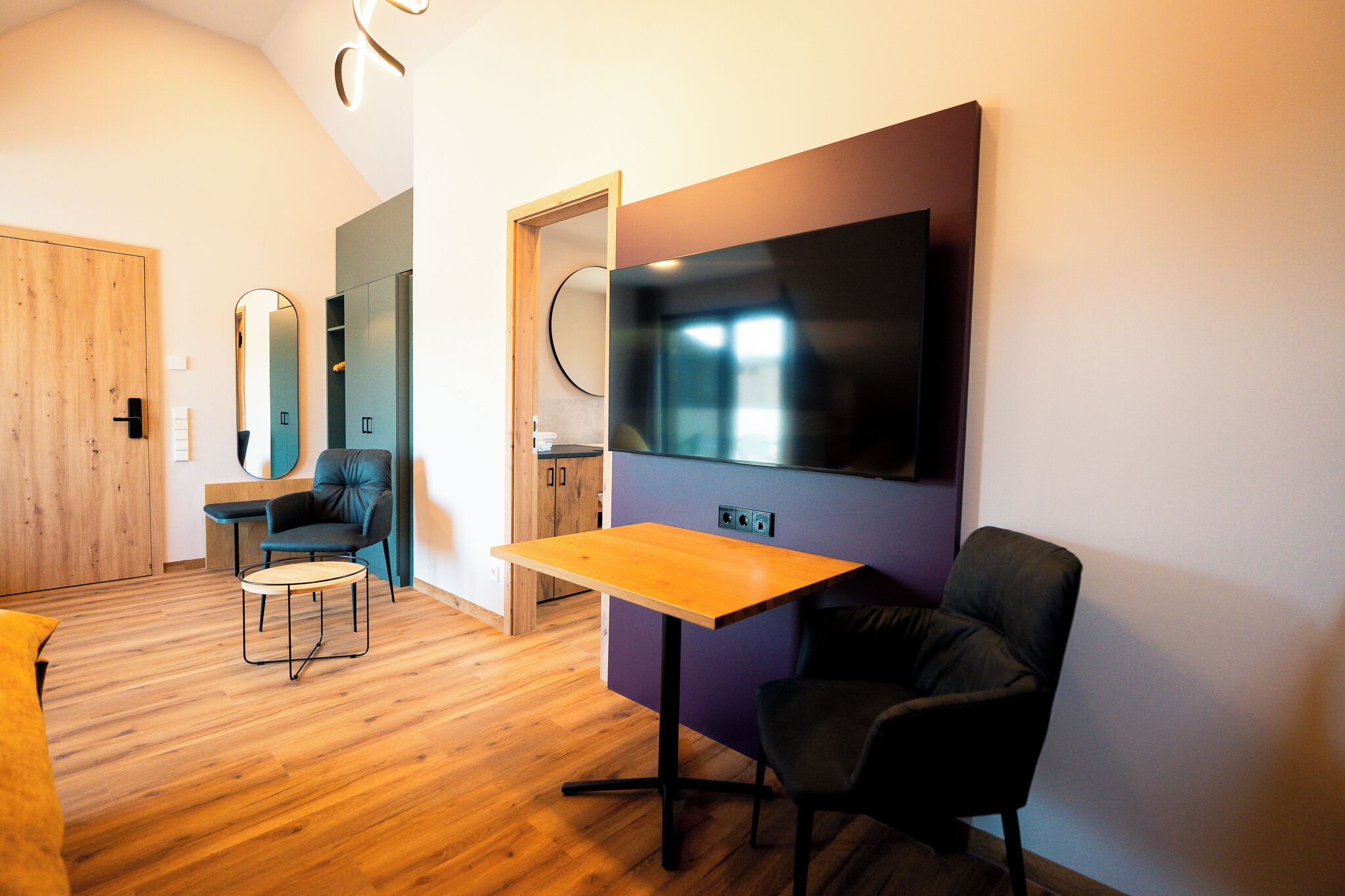 A modern living room with a flat-screen TV, a wooden table, and two chairs.