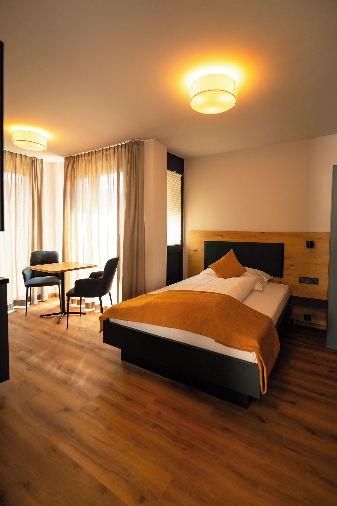 A hotel room with a wooden bed, a desk with chairs, and a window with curtains.