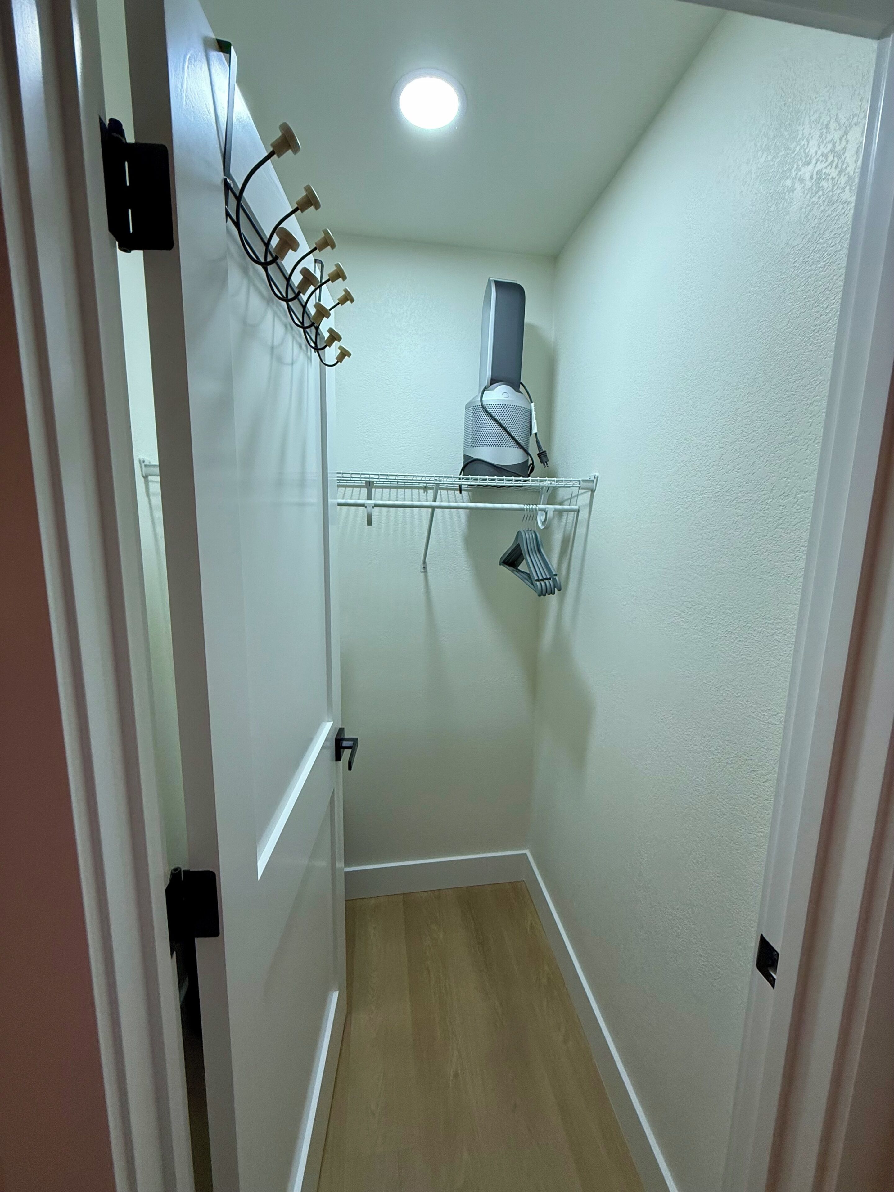 Ein schmaler Korridor mit einer weißen Tür links, einer weißen Wand und einer Deckenleuchte.