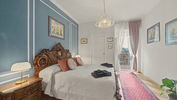 A bedroom with a large bed, a dresser, a chandelier, and a view of the outside.