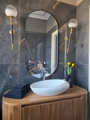 A bathroom with a round mirror, a white sink, and a wooden vanity.