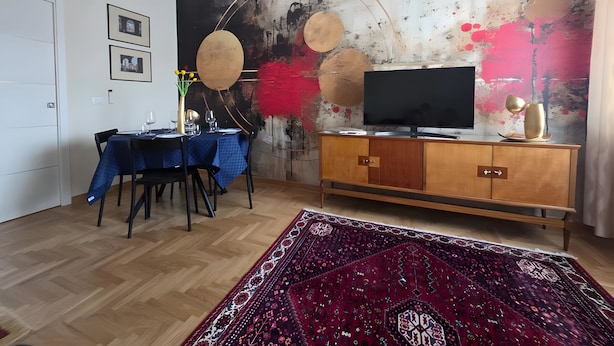 Ein modernes Wohnzimmer mit Essbereich, einem Flachbildfernseher, einer Holzkommode und einem großen abstrakten Gemälde an der Wand.