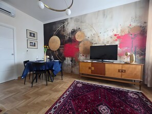 A modern living room with a dining area, a flat-screen TV, a wooden cabinet, and a large abstract painting on the wall.