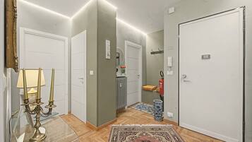 A hallway with a glass table, a candelabra, a rug, and a door with a fire extinguisher.
