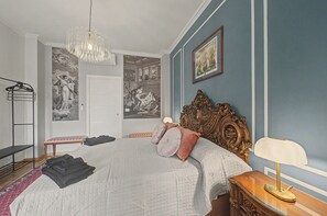 A bedroom with a large bed, a chandelier, a wooden headboard, and a framed picture on the wall.