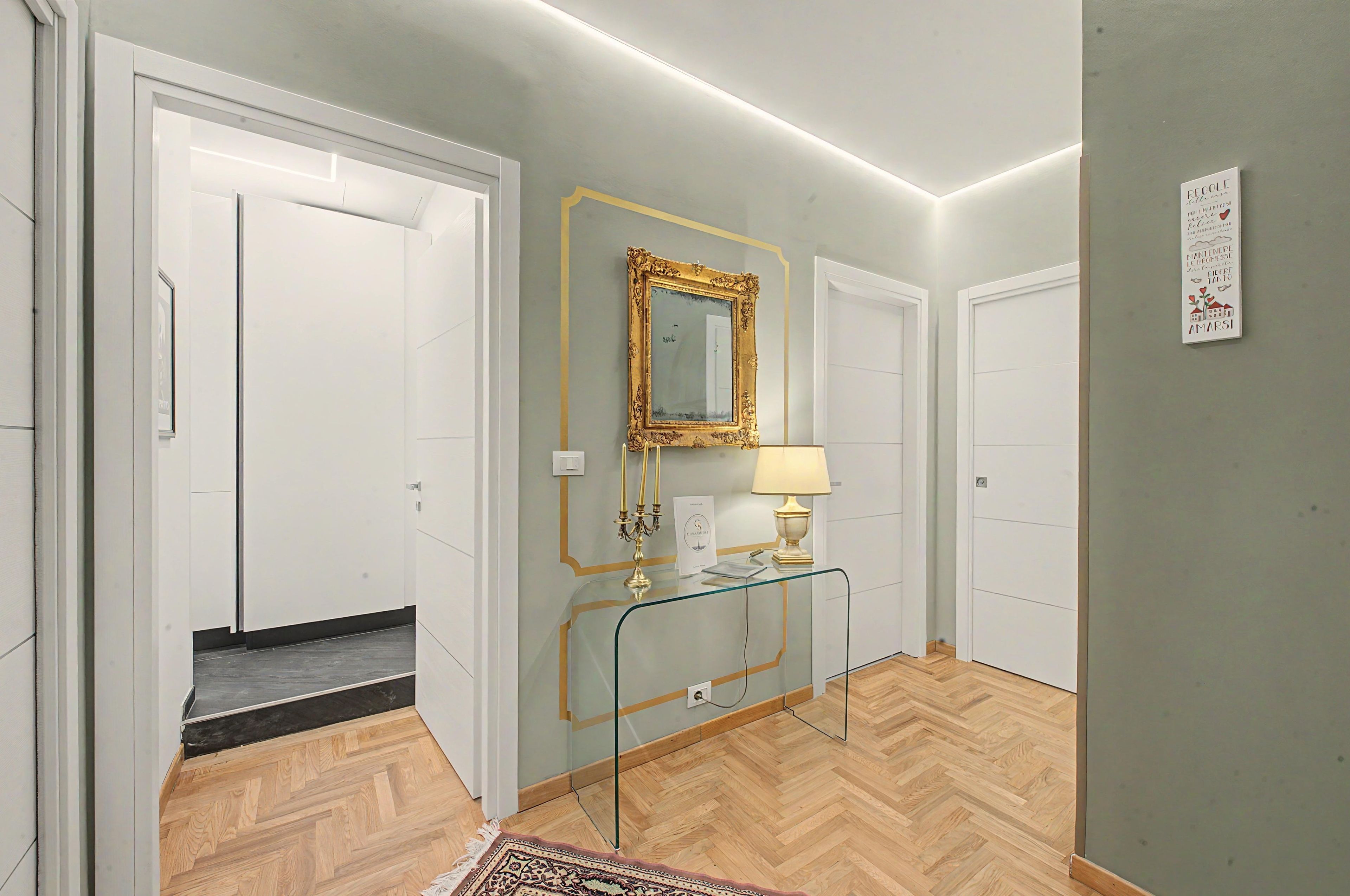 Ein Flur mit einem Glastisch, einem goldgerahmten Spiegel und einer Lampe. Auf beiden Seiten befinden sich weiße Türen.