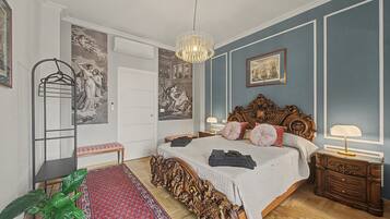 Un dormitorio con una cama grande, un cabecero ornamentado, una lámpara colgante, un tapete rojo estampado y una planta en maceta.