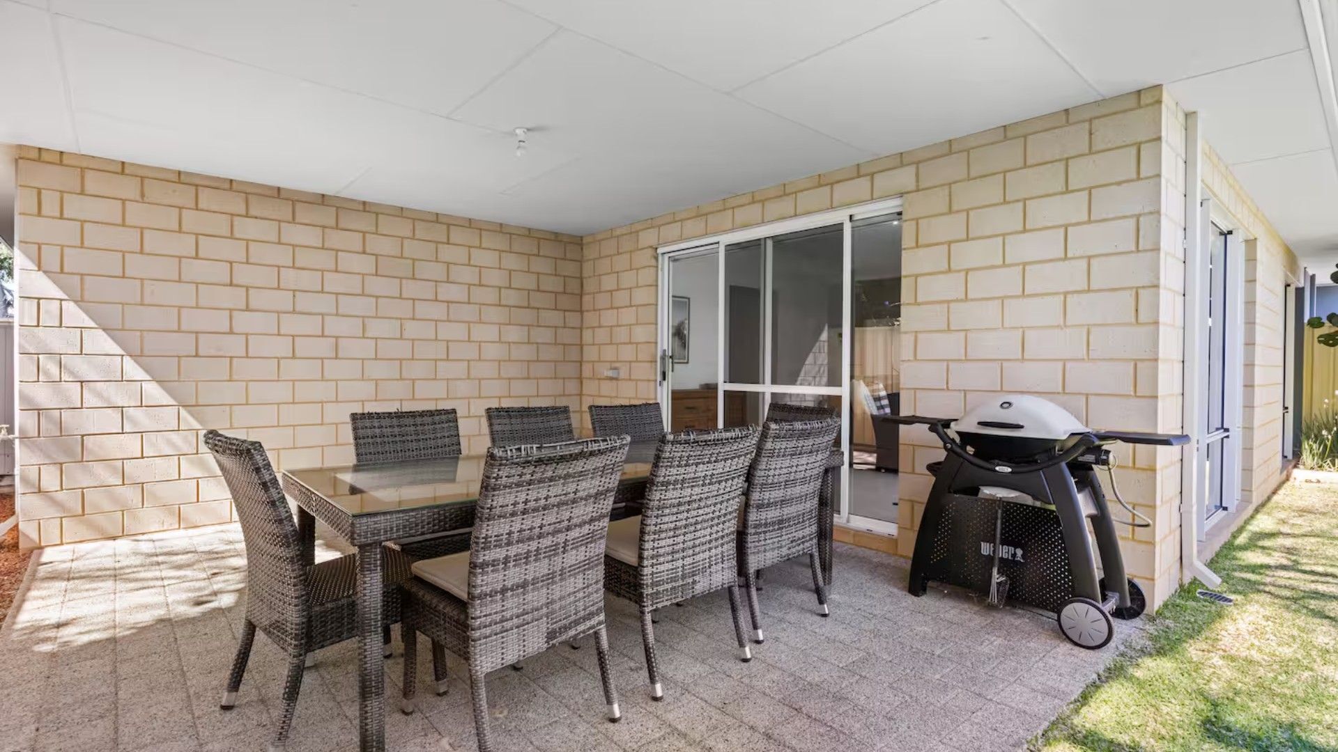 Un espace patio aménagé avec une table et des chaises, un barbecue et une porte-fenêtre coulissante.
